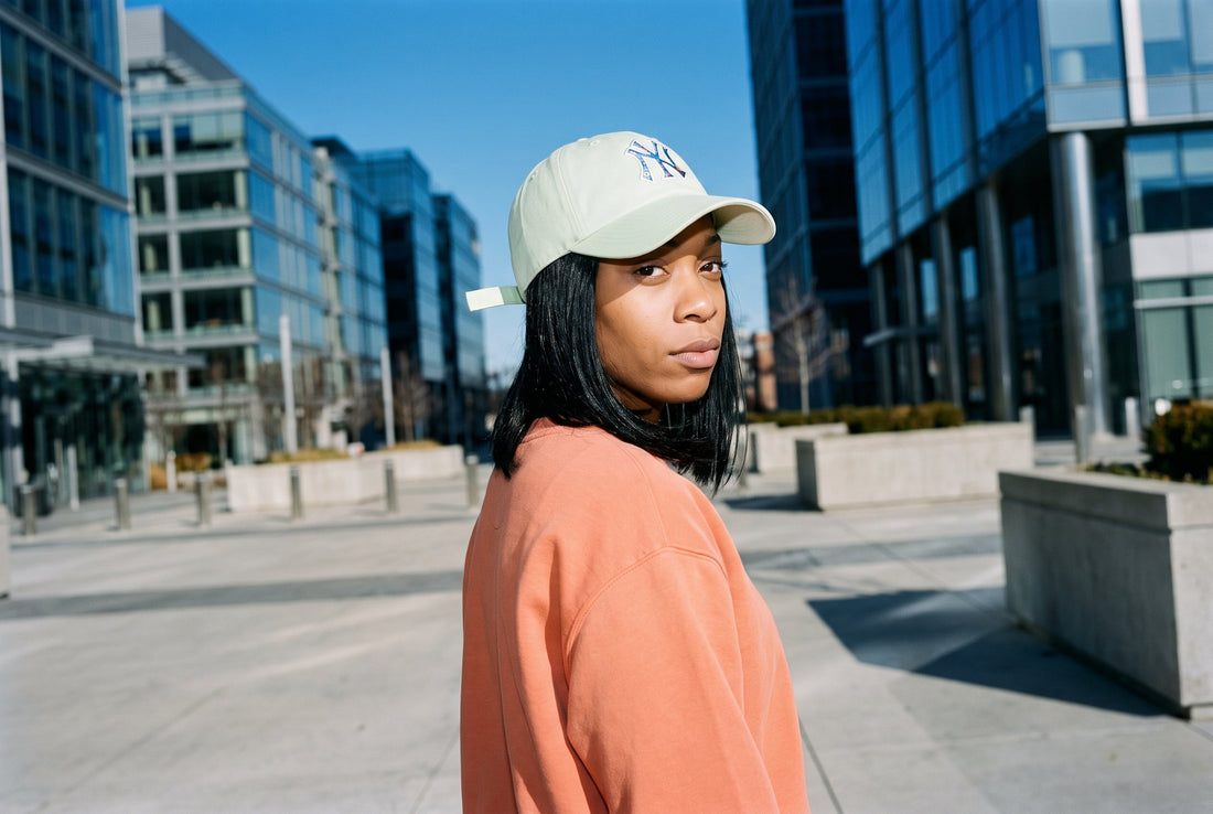 Frau mit mintgrüner '47 Yankees Cap und lachsfarbenem Sweatshirt auf einem modernen Stadtplatz