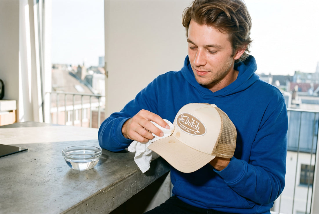 Mann tupft einen leichten Fleck auf seiner beigen Von Dutch Trucker Cap mit einem feuchten Baumwolltuch ab, daneben eine Schale mit Wasser