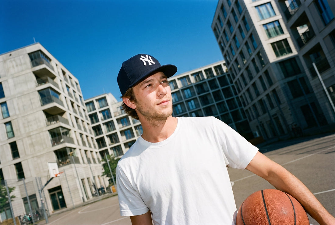 Mann mit marineblauer New Era 59FIFTY Yankees Cap und Basketball auf einem Streetball-Platz zwischen Wohnblöcken