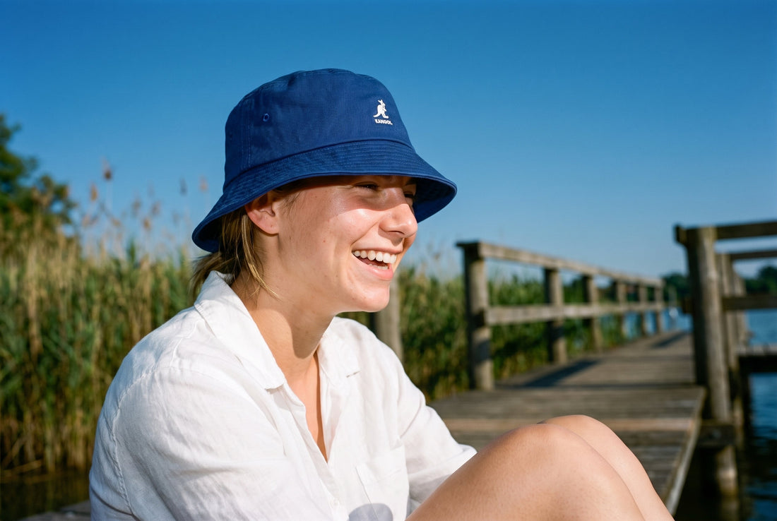 Lachende Frau mit royalblauem Kangol Washed Bucket Hat auf einem Steg am Badesee